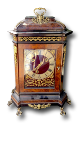 Pendule de table ancienne décorée, boîtier sombre avec ornements dorés, cadran rond, posée sur quatre pieds