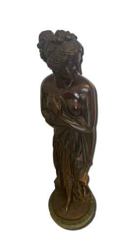 Sculpture en bronze figurative représentant une femme debout, tête tournée sur le côté, coiffure relevée et drapé tenu contre le buste, posée sur une base ronde avec socle vert.