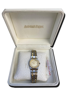 Montre vintage de luxe bicolore acier et or avec lunette sertie de pierres et cadran clair, posée dans un écrin blanc ouvert