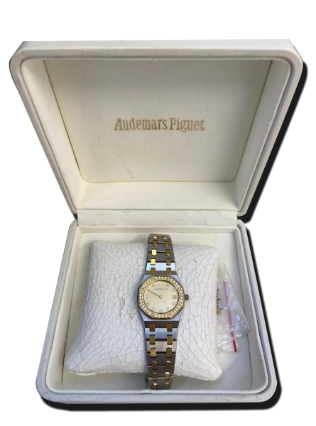 Montre vintage de luxe bicolore acier et or avec lunette sertie de pierres et cadran clair, posée dans un écrin blanc ouvert