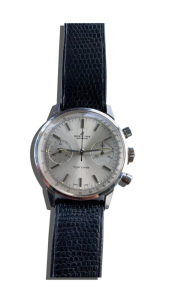 Montre vintage de luxe type chronographe avec cadran argenté, deux compteurs et bracelet en cuir bleu texturé ;