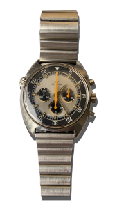 Montre vintage de luxe type chronographe en acier avec bracelet métal, cadran gris à trois compteurs, lunette noire graduée et détails orange ; Valais, Suisse.