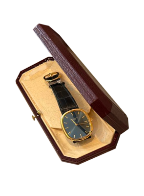 Montre de luxe vintage avec cadran foncé, boîtier doré et bracelet en cuir présentée dans son écrin d’origine.