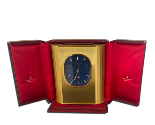 Pendulette de luxe dans son écrin rouge, boîtier doré et cadran bleu ovale avec index fins.